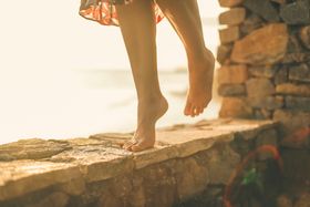 A woman balances barefoot on a stone wall by the sea during a serene evening in Weligama, Sri Lanka.