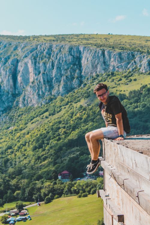 Free Man enjoys scenic mountain view sitting on cliff, capturing adventure and freedom. Stock Photo
