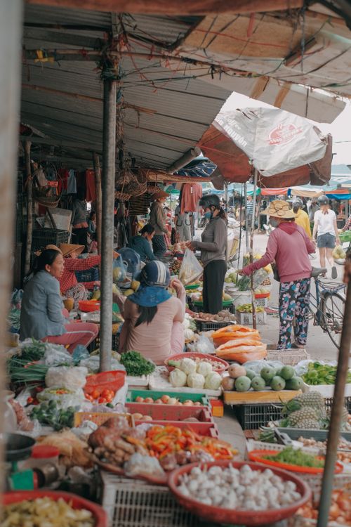 Free Bustling outdoor market with diverse people selling fresh produce under a canopy. Stock Photo