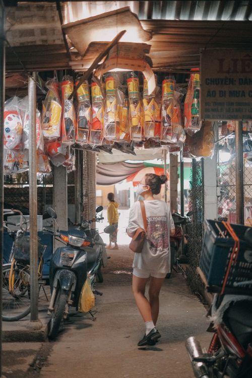 Free Woman in white shirt exploring a vibrant outdoor market alley lined with colorful goods and bicycles. Stock Photo