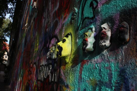 Dynamic street art featuring colorful graffiti and 3D masks on a textured wall.