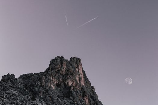 夜晚的天空中，戏剧性的山峰映衬着月亮和飞机的轨迹