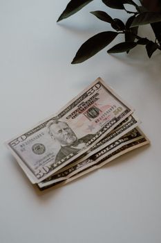 Stack of fifty dollar bills on a white background with green leaves. Perfect for finance or economy themes.