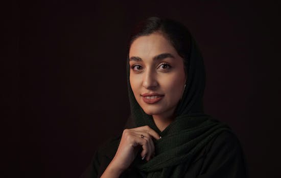 Beautiful portrait of a smiling woman in a dark green headscarf, set against a dark background.