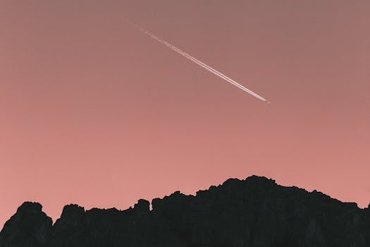 A scenic silhouette of mountains with a jet airplane streaking across the pink twilight sky.
