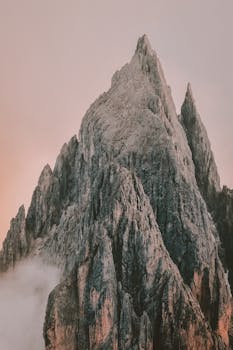 Dramatic mountain peaks emerging from morning mist under a serene sunrise sky.