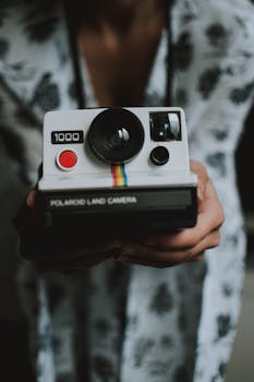 A close-up of a vintage Polaroid camera being held by a person, showcasing retro photography style.