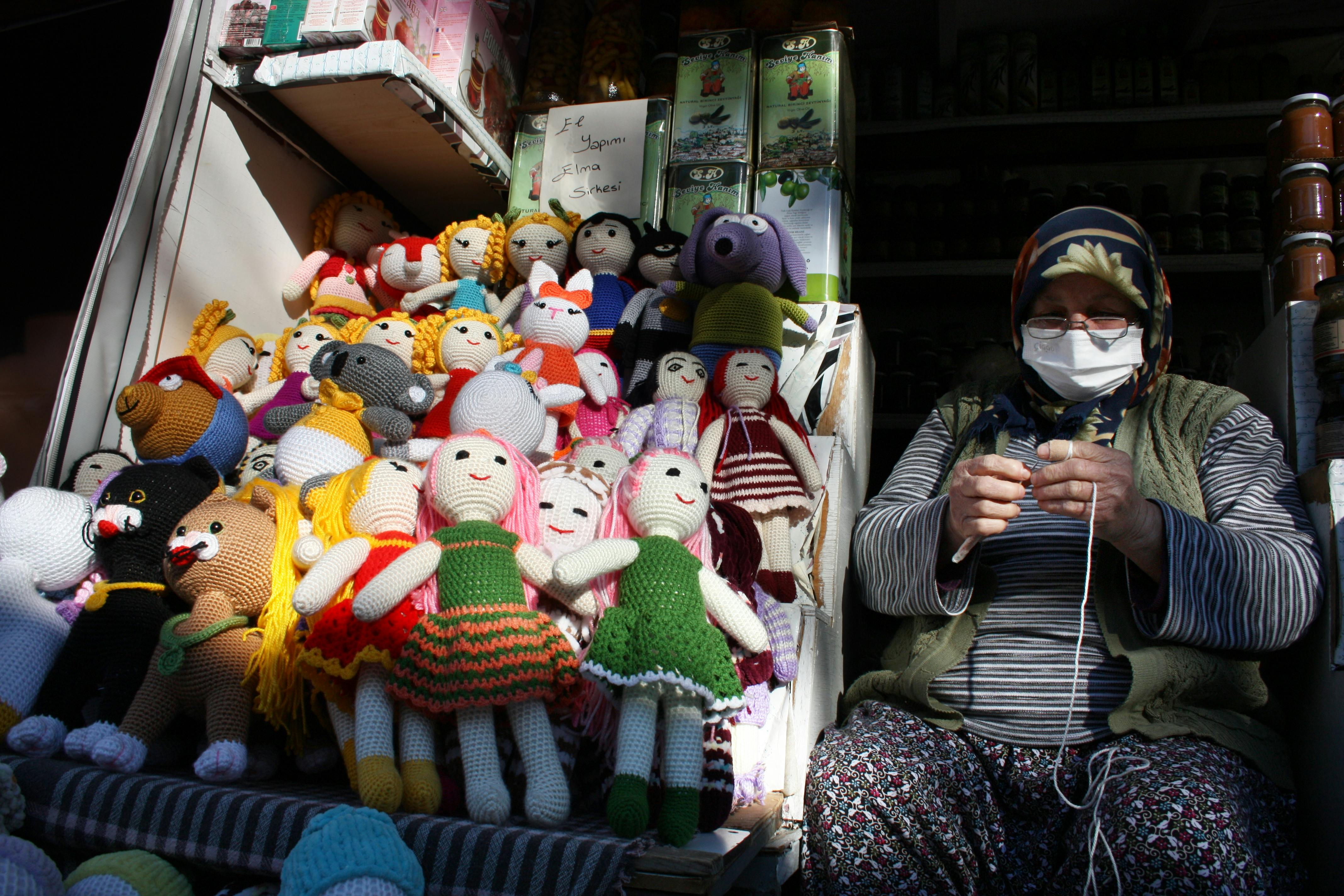 elderly woman knitting and selling handmade crocheted dolls at a stall