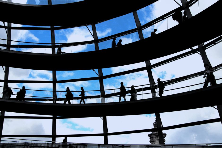 Siluetas de personas caminando dentro de la cúpula de vidrio del Reichstag en Berlín, Alemania, mostrando belleza arquitectónica.