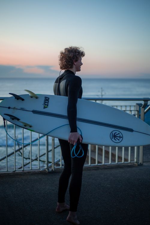 Free Surfer in a wetsuit holding a surfboard at sunrise by the ocean. Stock Photo