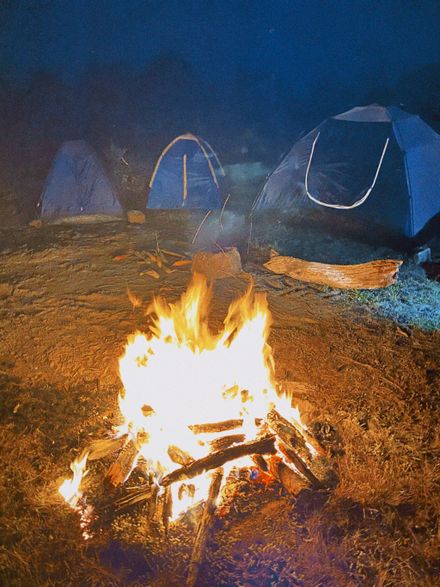Campfire burning beside tents after dark — photo by Priscila Almeida on Pexels