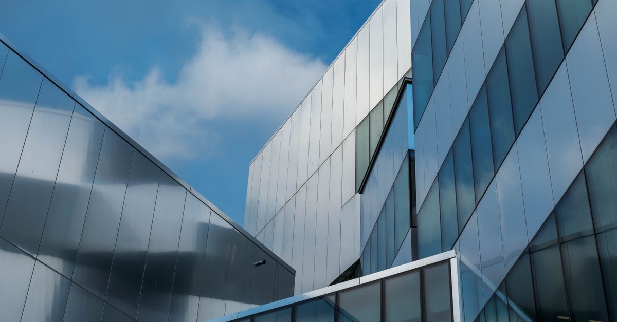 Low angle view of modern glass buildings reflecting blue sky and clouds.