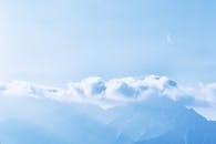 群山笼罩在云雾之中，蔚蓝的天空中挂着一轮新月