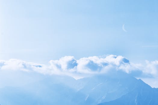 群山笼罩在云雾之中，蔚蓝的天空中挂着一轮新月