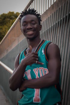 Black man smiling in a New York jersey, enjoying a sunny day outdoors.