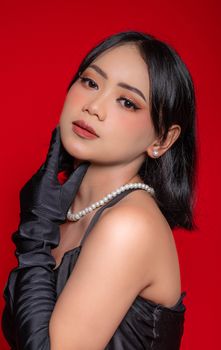 Stylish portrait of a woman wearing pearls and black opera gloves against a red background.