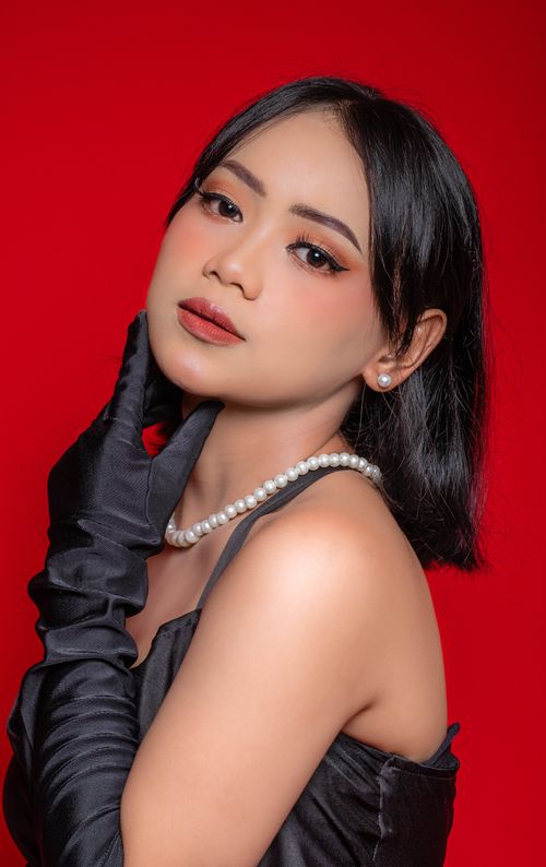 Free Stylish portrait of a woman wearing pearls and black opera gloves against a red background. Stock Photo