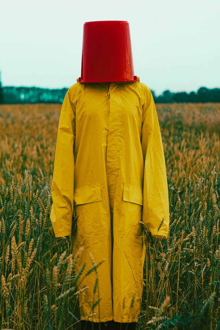 Person In Yellow Coat And Bucket On Head In Field