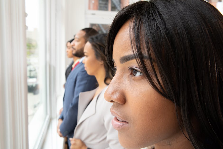 Focused professionals stand by a window, looking out with determination. Teamwork in a modern office.
