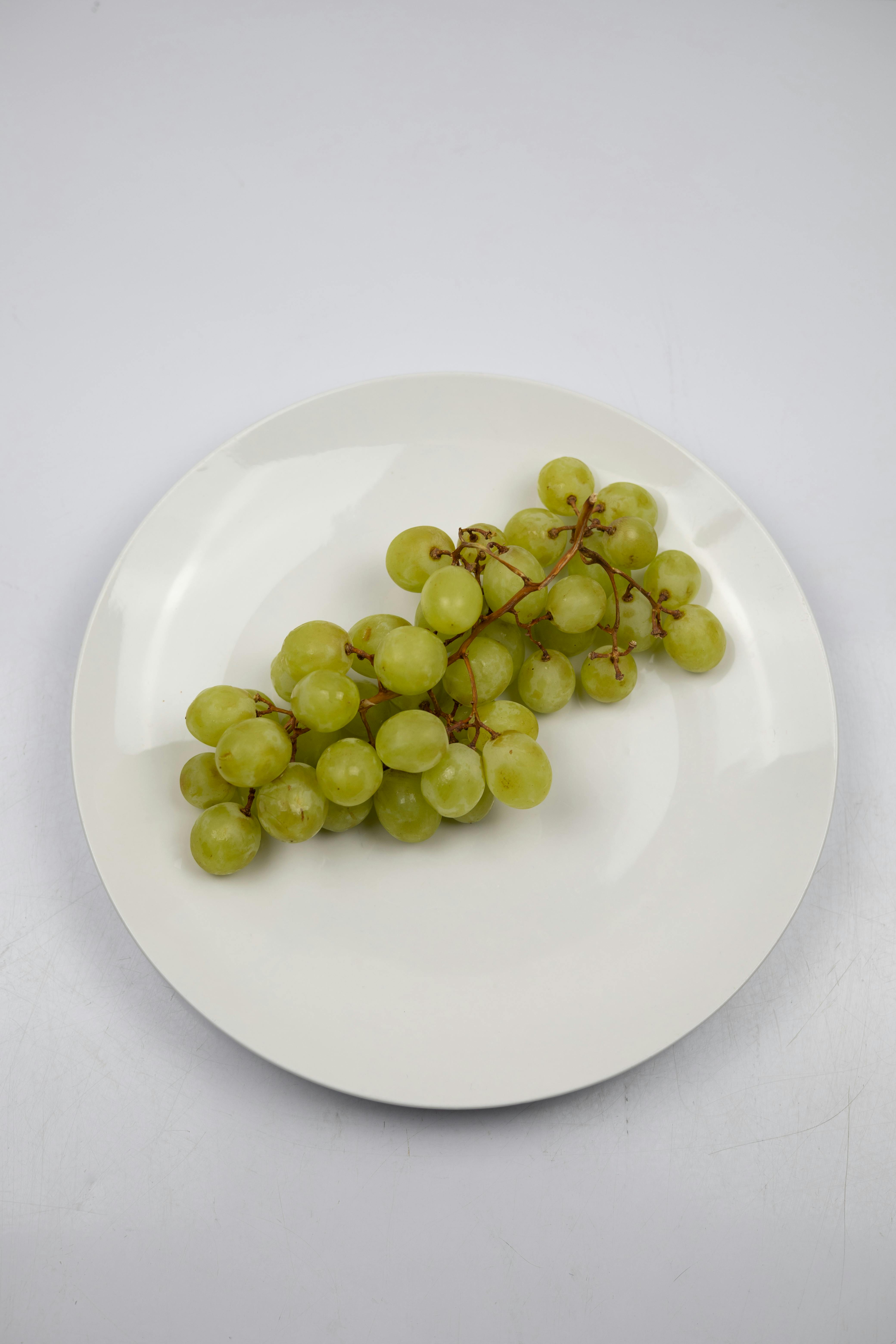 A cluster of fresh green grapes on a white plate, perfect for healthy snacking or culinary use.