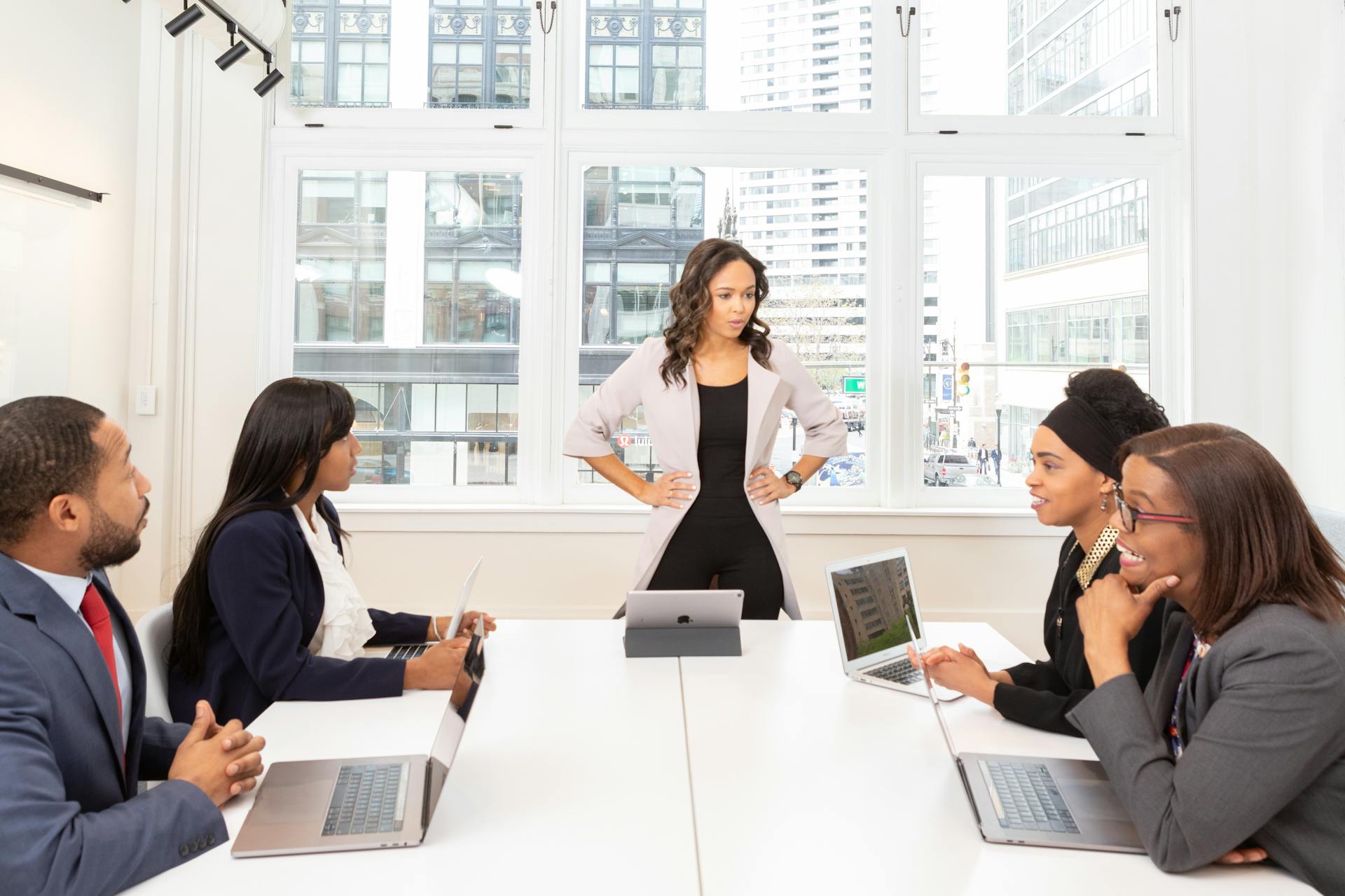 A diverse group of professionals engaged in a meeting at a modern office with laptops and city view.