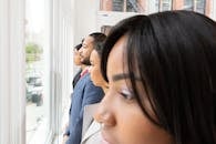 一群多元化的商业专业人士若有所思地从办公室窗户向外张望