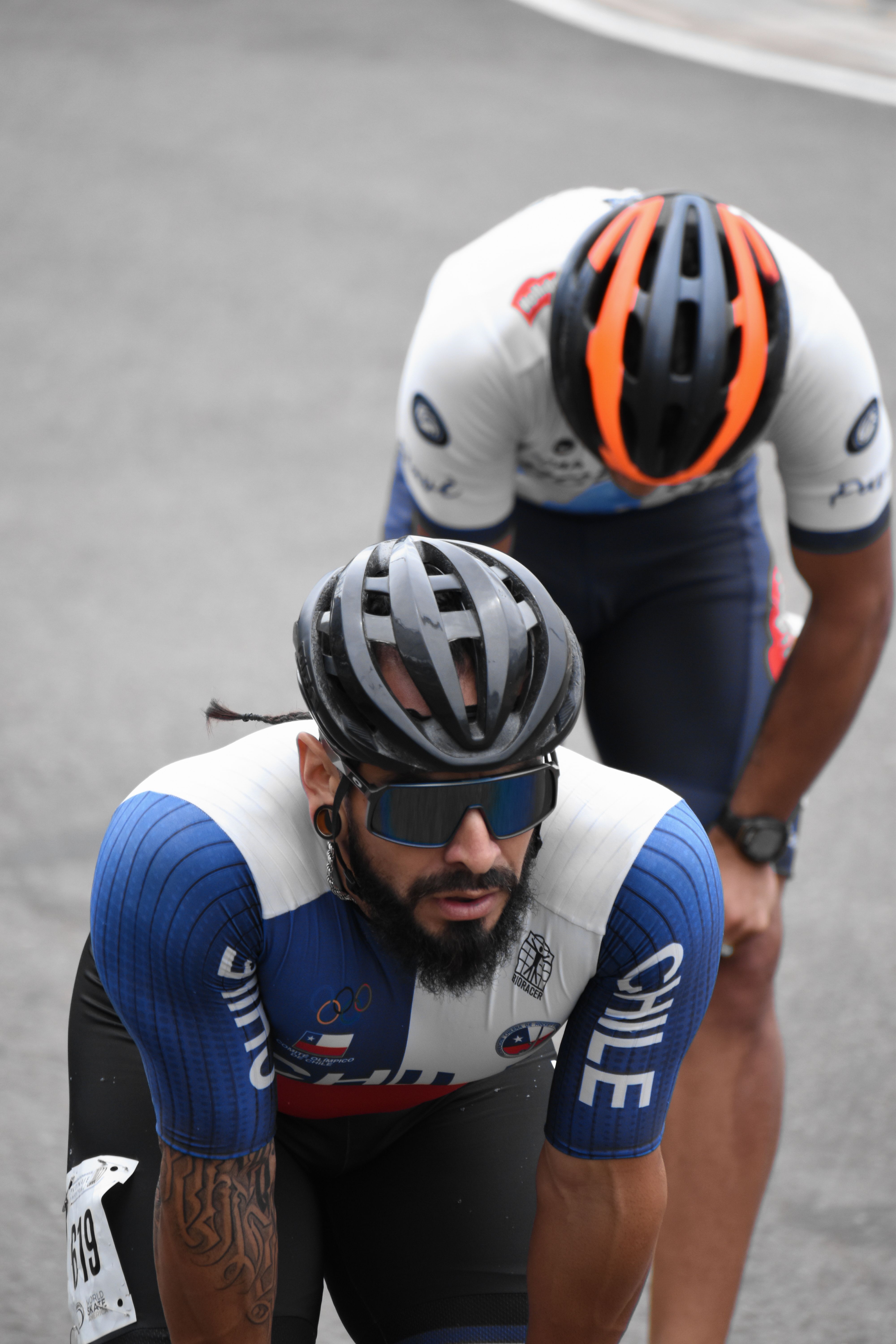 Two male cyclists with helmets prepare for a competition on an outdoor track in Ibagué, Colombia.