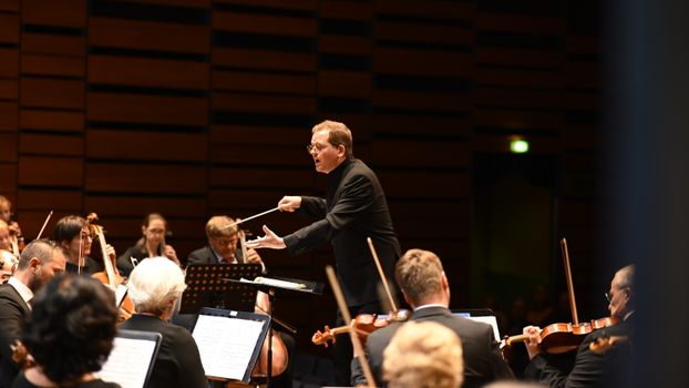 Orchestra conductor leading a live classical music performance indoors.