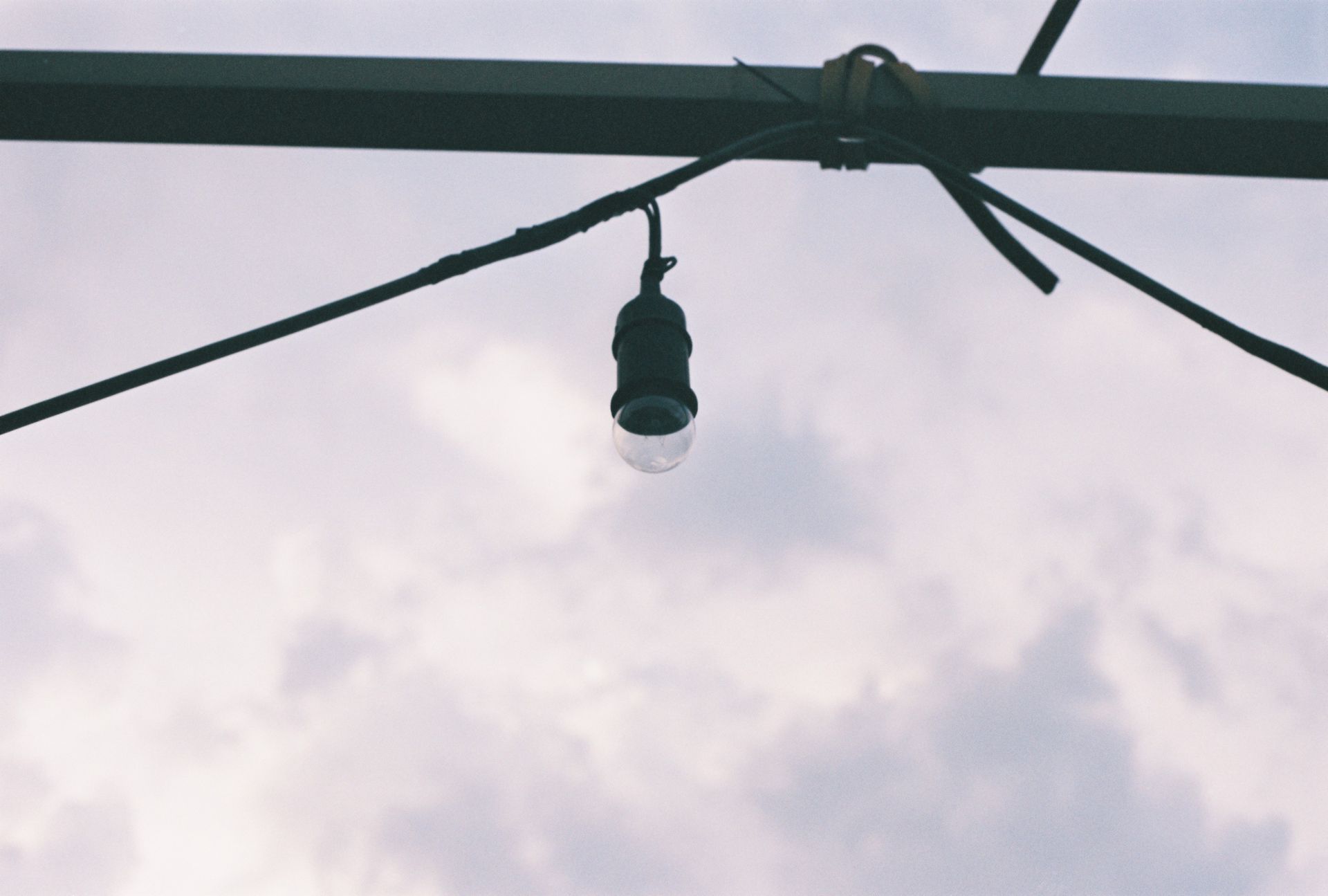 A simple light bulb hanging from a wire, silhouetted against a cloudy sky.