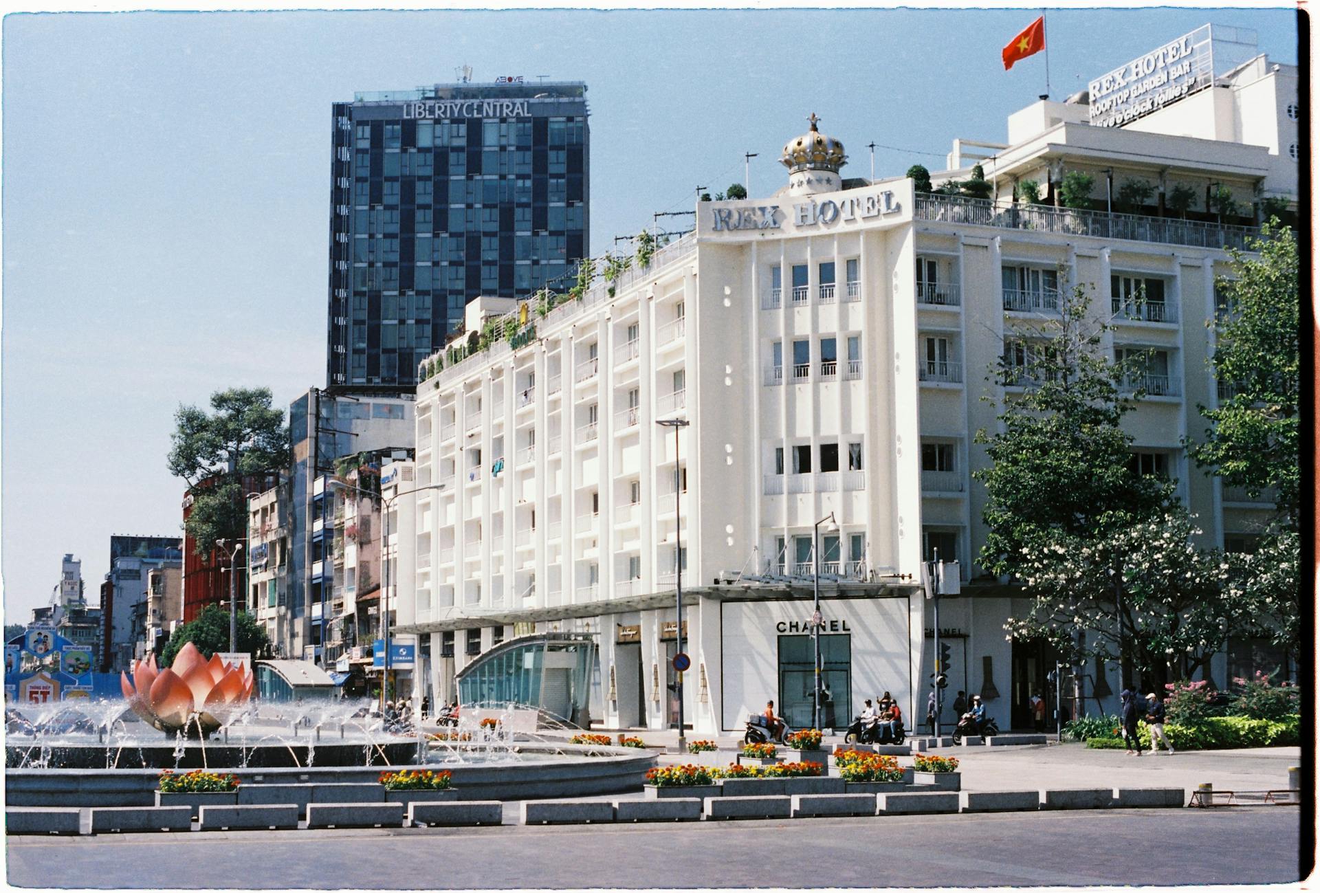 View of Rex Hotel and surrounding cityscape in Ho Chi Minh City with a fountain in the foreground.