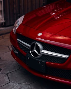 Close-up of a red Mercedes Benz hood showing the iconic emblem and front grill in an urban setting.