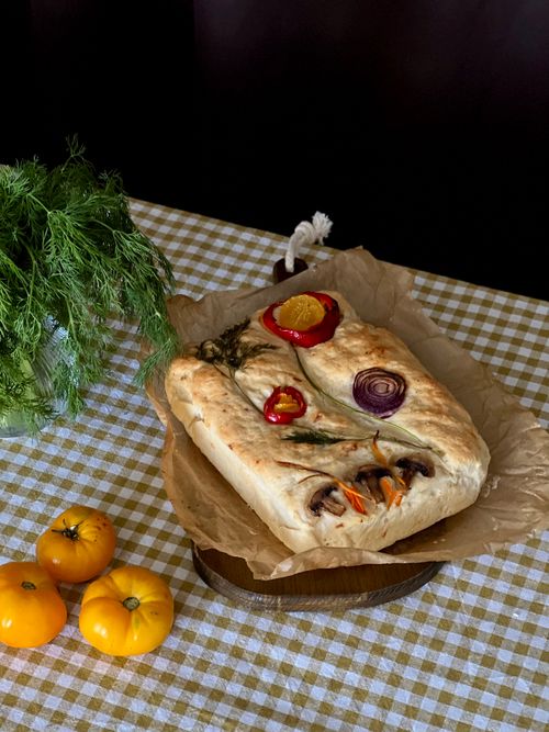 Free Delicious homemade focaccia topped with fresh vegetables and herbs on a rustic table. Stock Photo