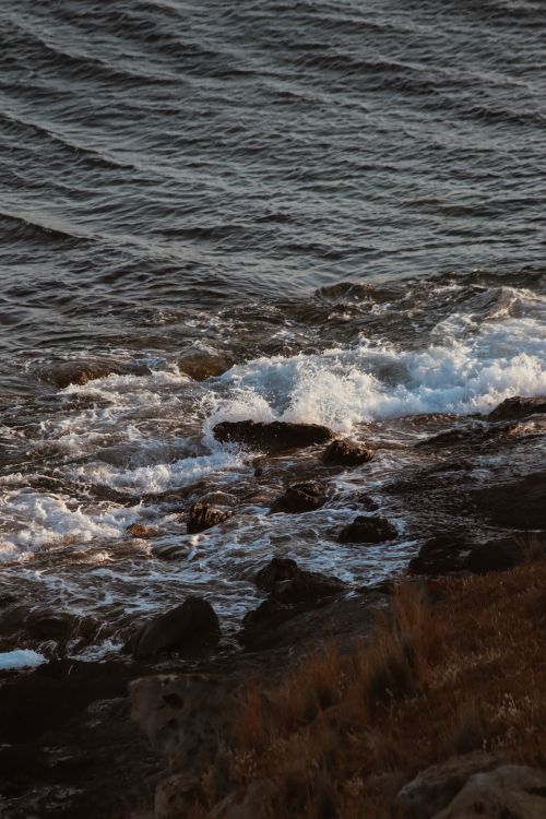 Free Waves crashing on a rocky shoreline, creating a dynamic seascape in natural light. Stock Photo