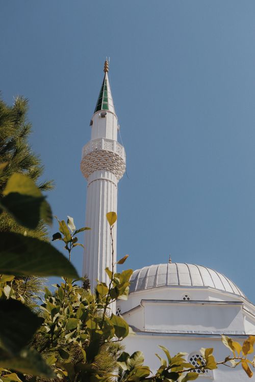 Free A striking mosque minaret with a dome surrounded by lush greenery under a clear blue sky. Stock Photo