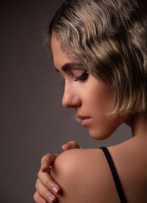 Free Profile portrait of a woman with short hair touching her shoulder, in a soft and moody setting. Stock Photo