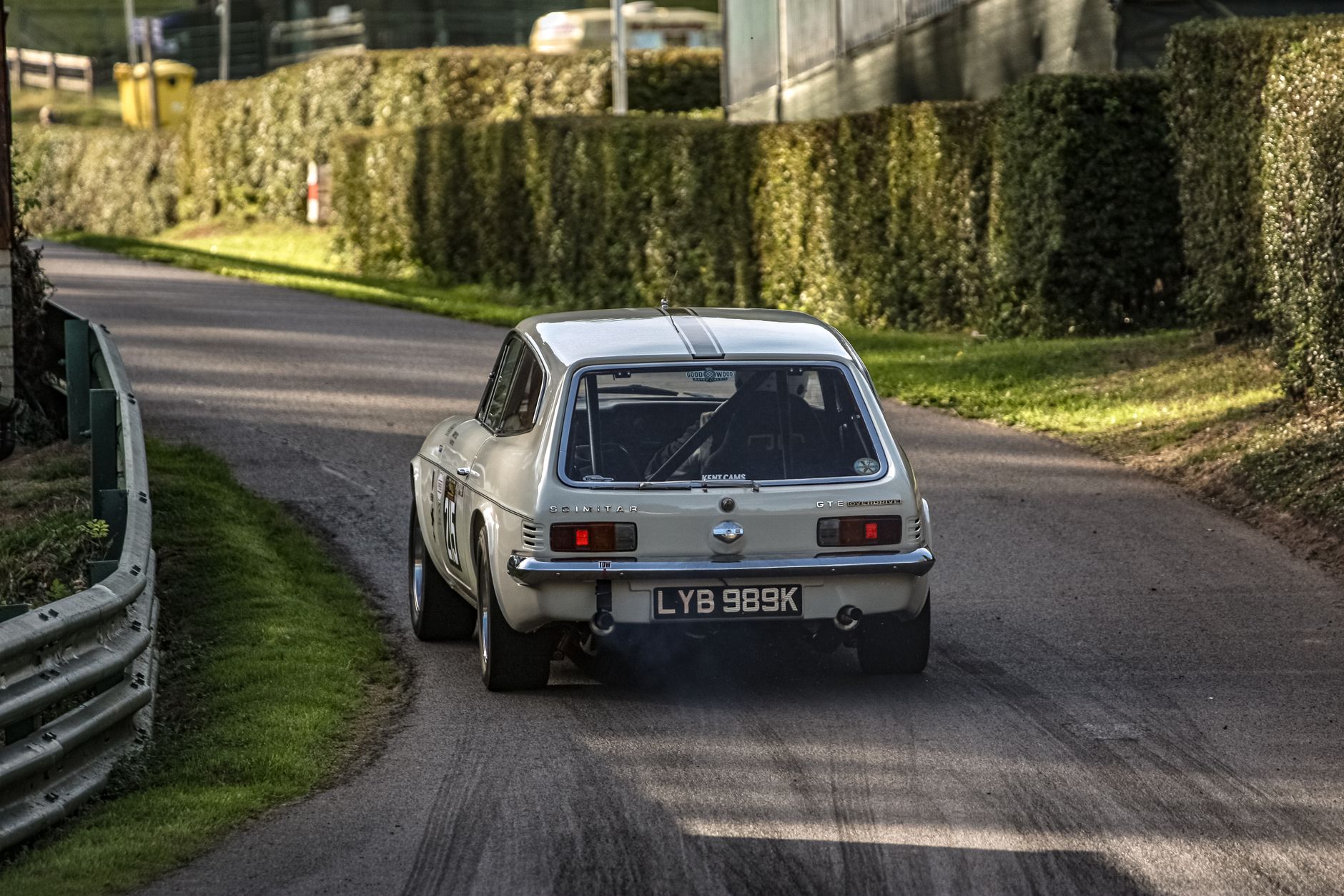 A vintage Reliant Scimitar racing through a scenic road surrounded by hedges.