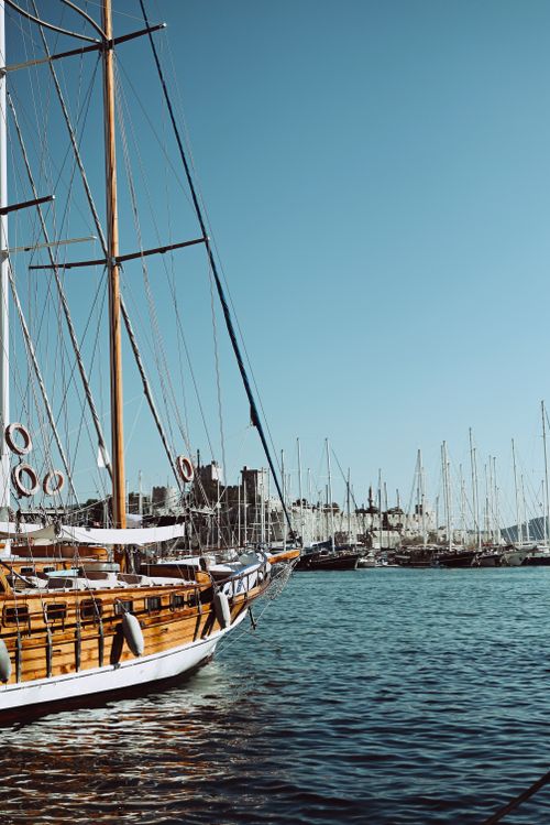 Free Wooden sailboat in a vibrant marina with clear blue sky and calm waters. Stock Photo