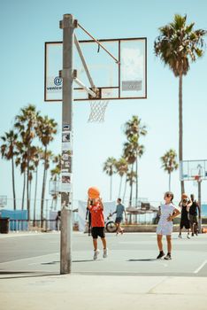 Two kids enjoying a basketball game at sunny Venice Beach with palm trees.
