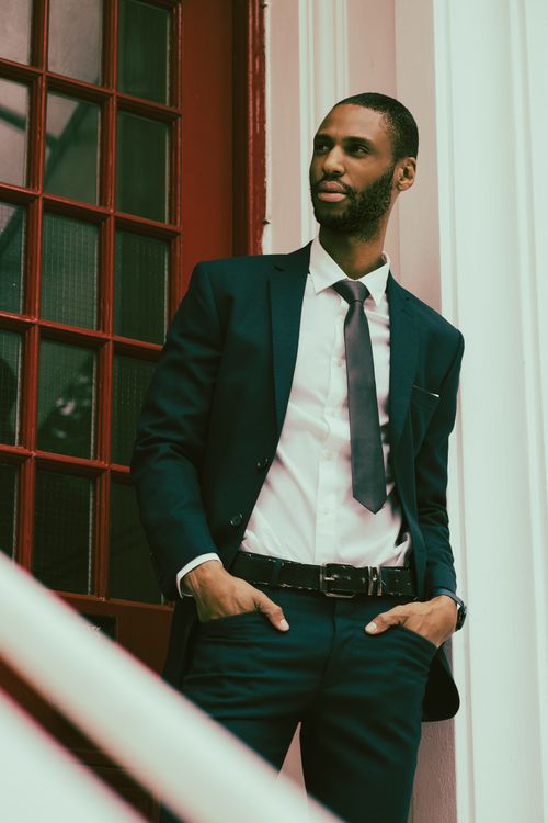 Free Stylish African American man in a suit posing confidently by a red door. Stock Photo