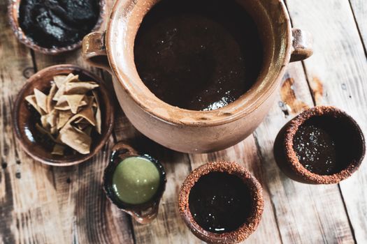 A top view of traditional Mexican beverages and snacks in clay pots and bowls on a rustic wooden table.