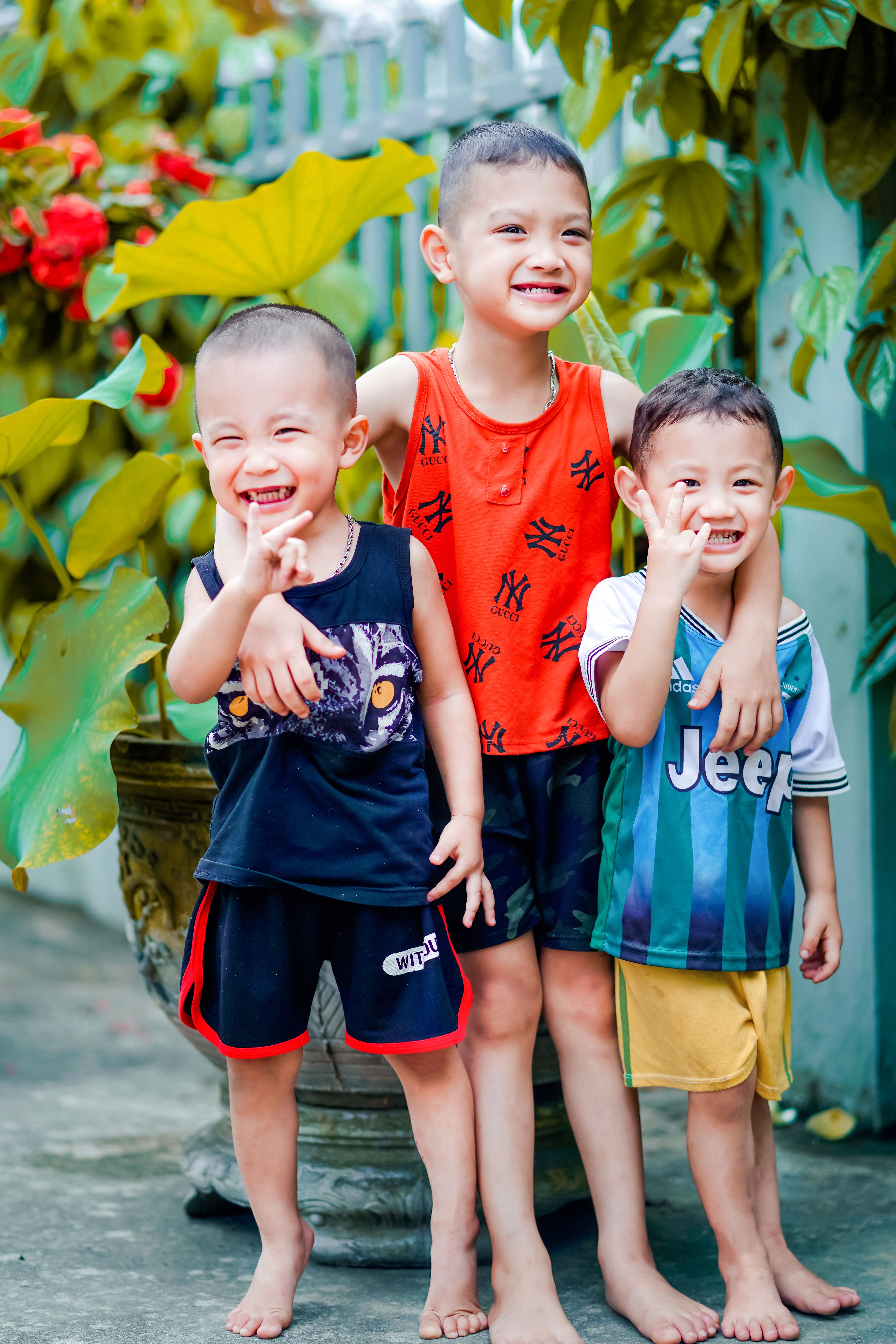 Three joyful siblings smiling and posing outdoors surrounded by greenery, embodying happiness and togetherness.