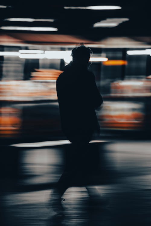 Man in Black Coat Standing on Sidewalk during Night Time