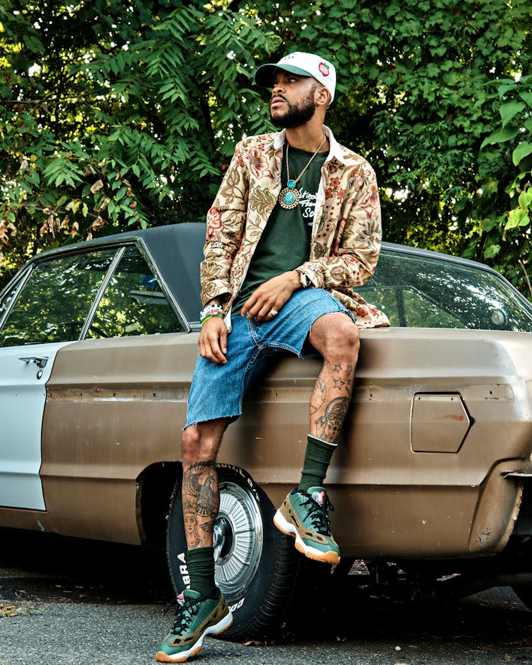 Man With Tattoos Sitting On Car