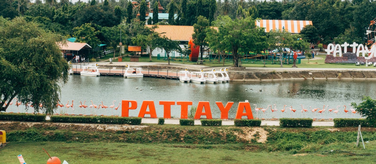 A vibrant scene in Pattaya, Thailand with a lake, iconic sign, and colorful decorations.