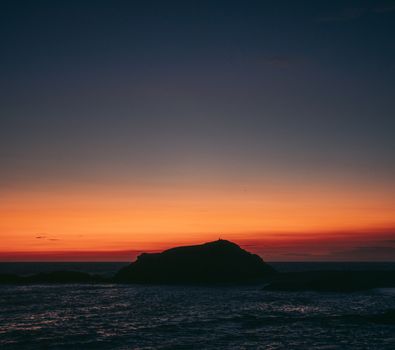 Sky ablaze with colors as the sun sets over a serene ocean and silhouetted island.