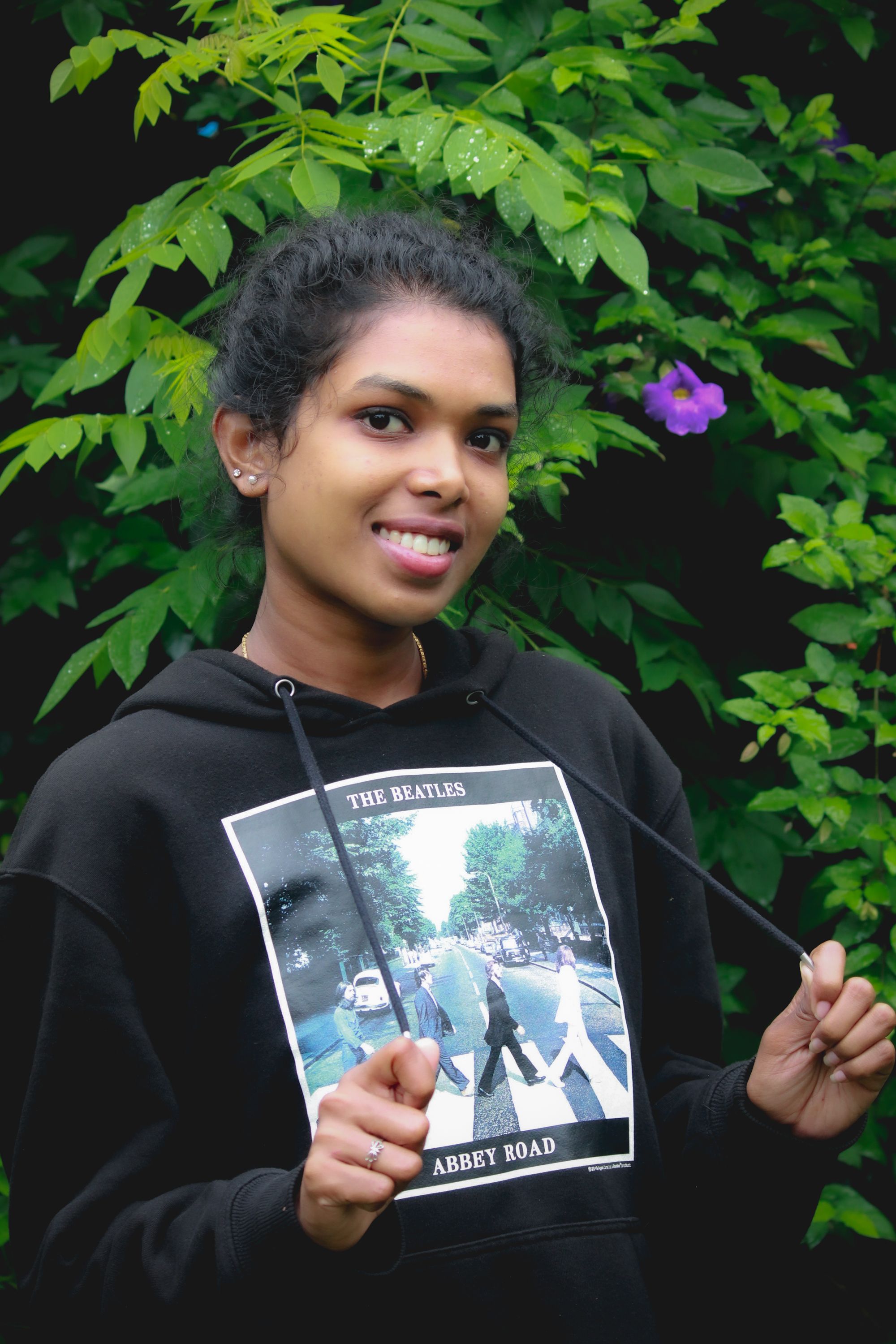 Portrait of a smiling woman in a black hoodie amidst lush greenery in Madikeri, India