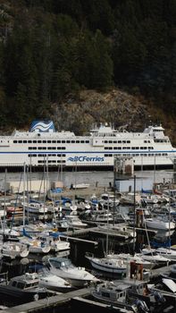 A BC Ferries vessel docked near a bustling marina with numerous boats.