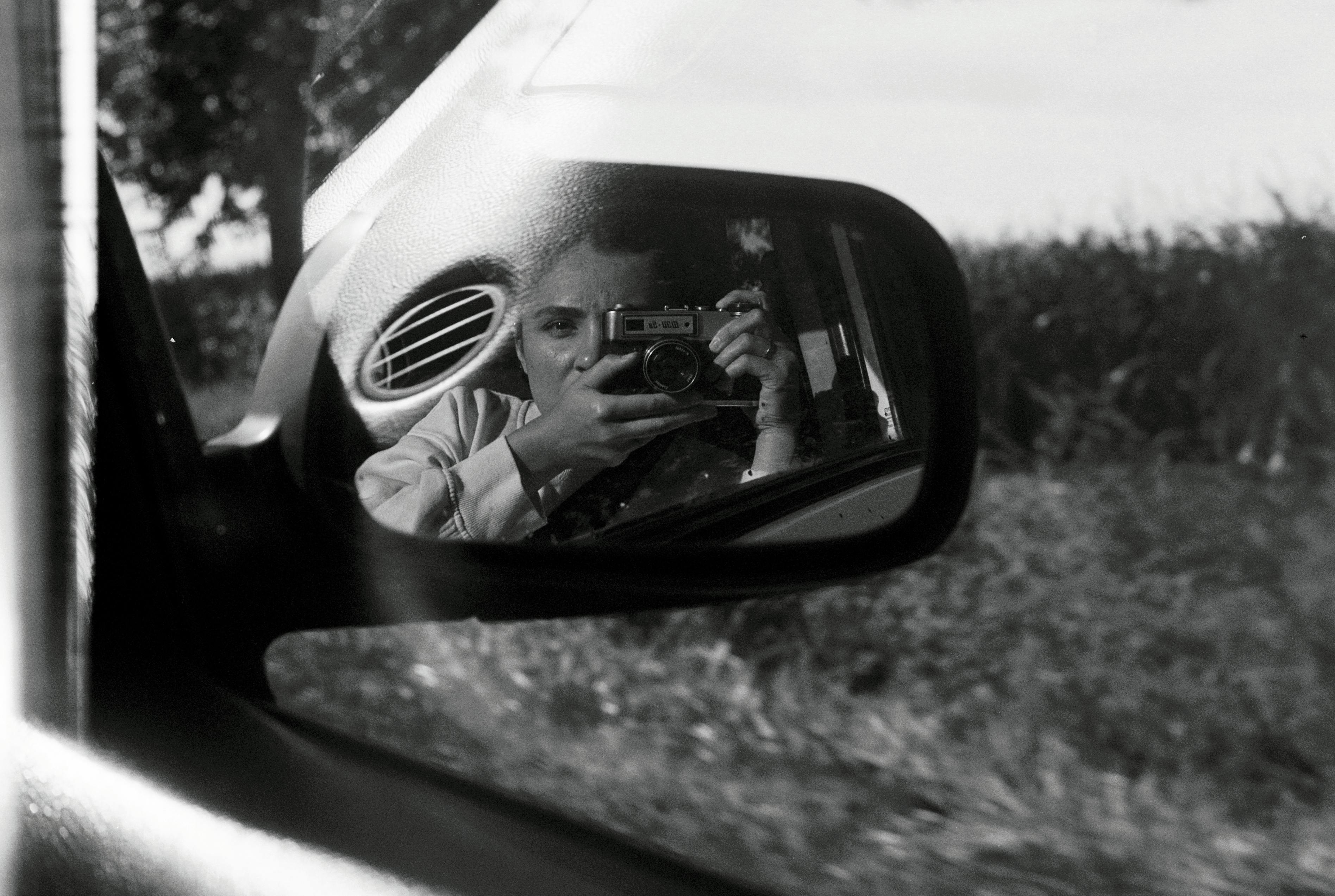 A person takes a photo through a car side mirror in monochrome style.