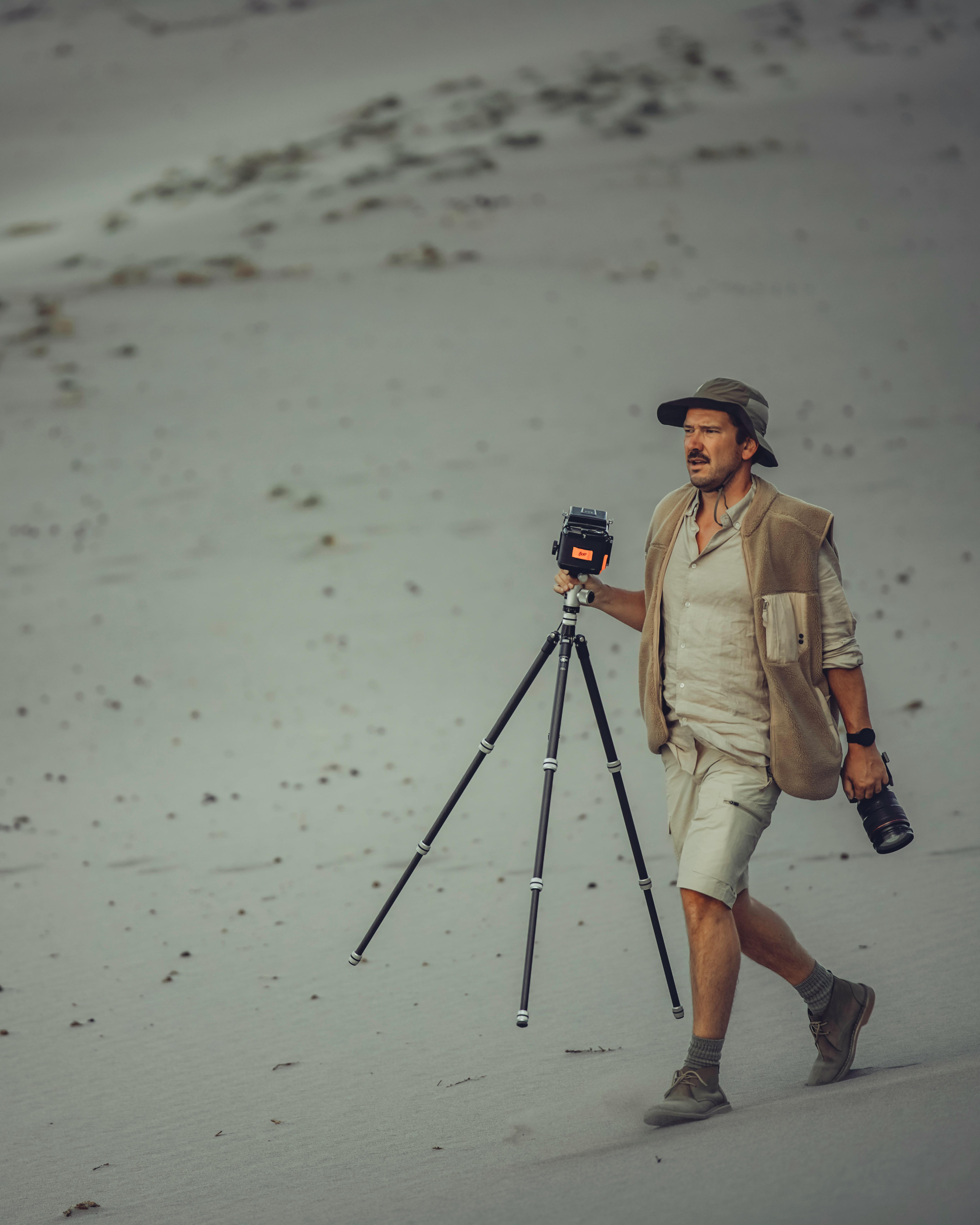 A man walking in the desert carrying a camera and tripod, showcasing outdoor photography.