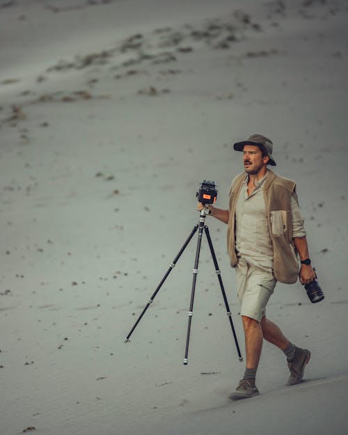A Photographer Walking while Holding a Tripod